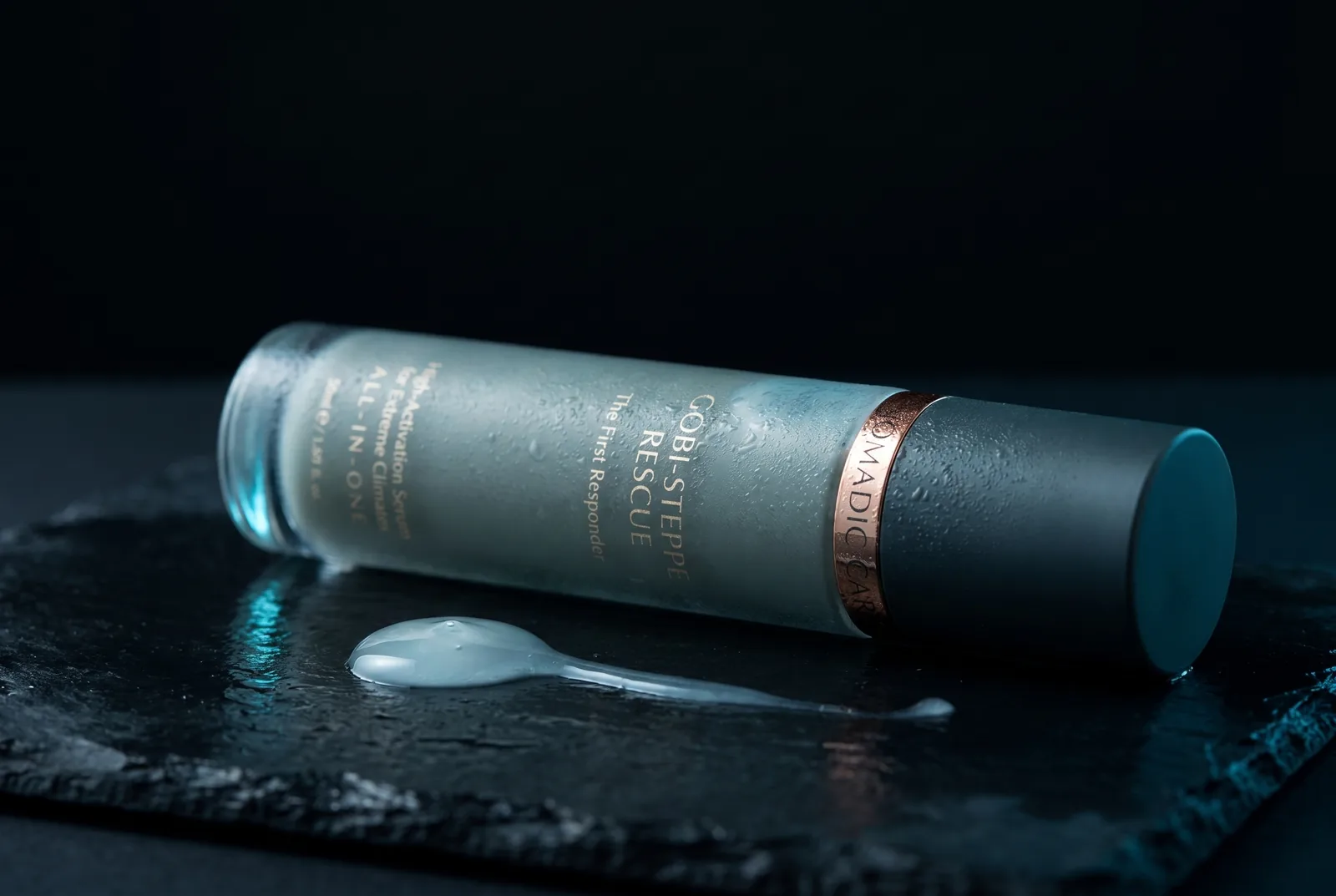 The Gobi-Steppe Rescue bottle resting on its side on wet black slate beside a glossy serum droplet, in cold glacial light